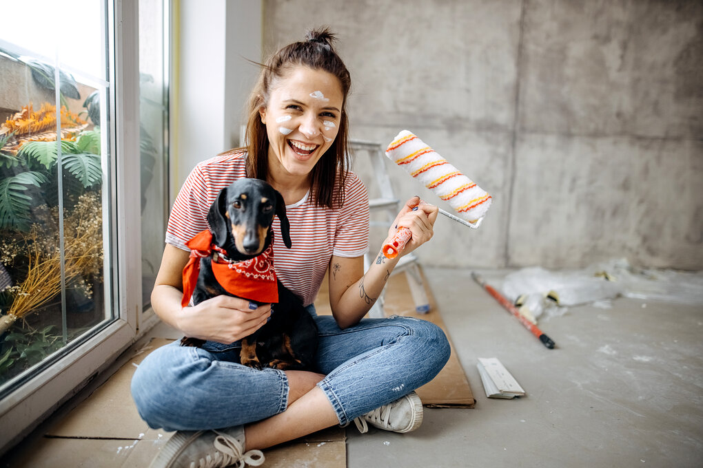 A woman smiling in the middle of painting her home with her dog 